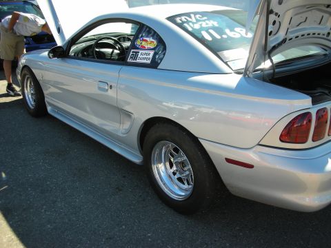 1998 Ford Crown Victoria - Silver Ford Mustang coupe shown in profile with polished drag wheels and an open trunk at an outdoor event.