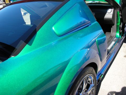 1998 Ford Crown Victoria - Close-up of color-shifting blue-green metallic flake paint on a car's side panel, mirror and rear wheel.