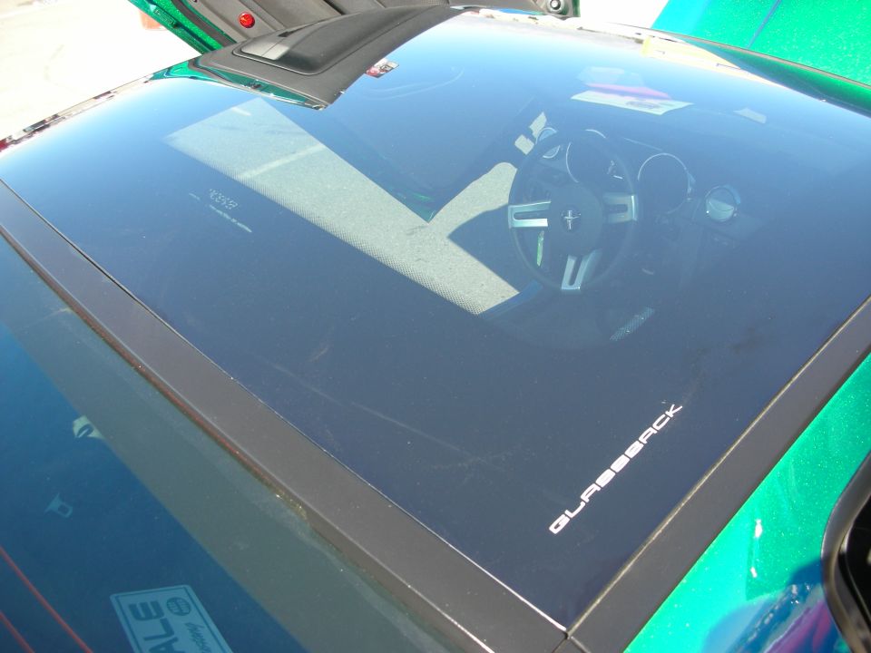 Glass rear hatch over a car interior with Mustang gauge cluster reflected