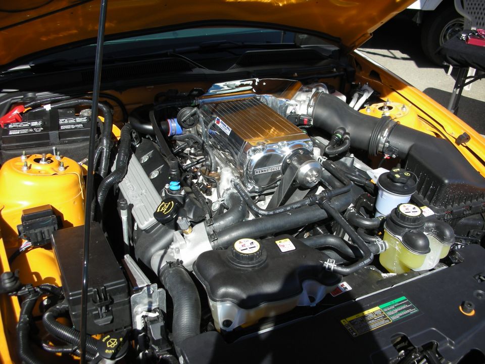 Engine bay of an orange Mustang with supercharger and intake