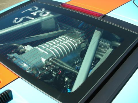 1998 Ford Crown Victoria - Supercharged mid-mounted engine viewed through a clear rear window on a light-blue and orange car.