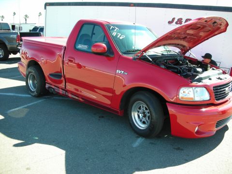 1998 Ford Crown Victoria - red Ford F-150 SVT Lightning regular-cab pickup sits in a paved lot with its hood raised, wearing drag wheels and a race number on the wind…