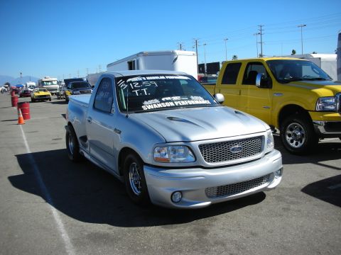 1998 Ford Crown Victoria - silver Ford regular-cab pickup with a raised cowl hood, lowered stance, and polished drag wheels parked near a yellow SUV.