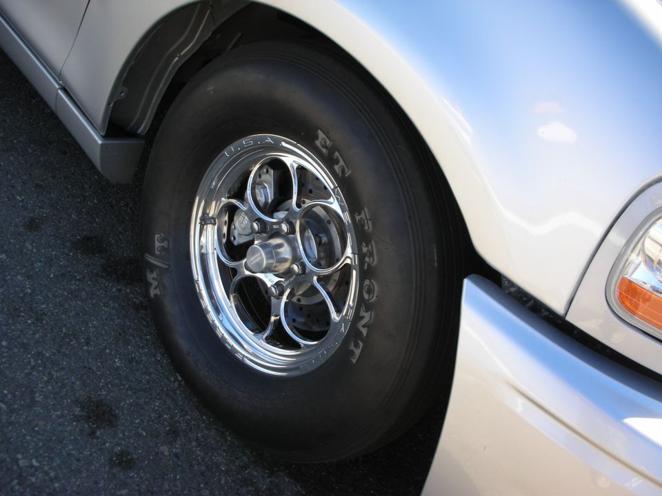 Close-up of a polished front drag wheel and slick tire on a silver vehicle