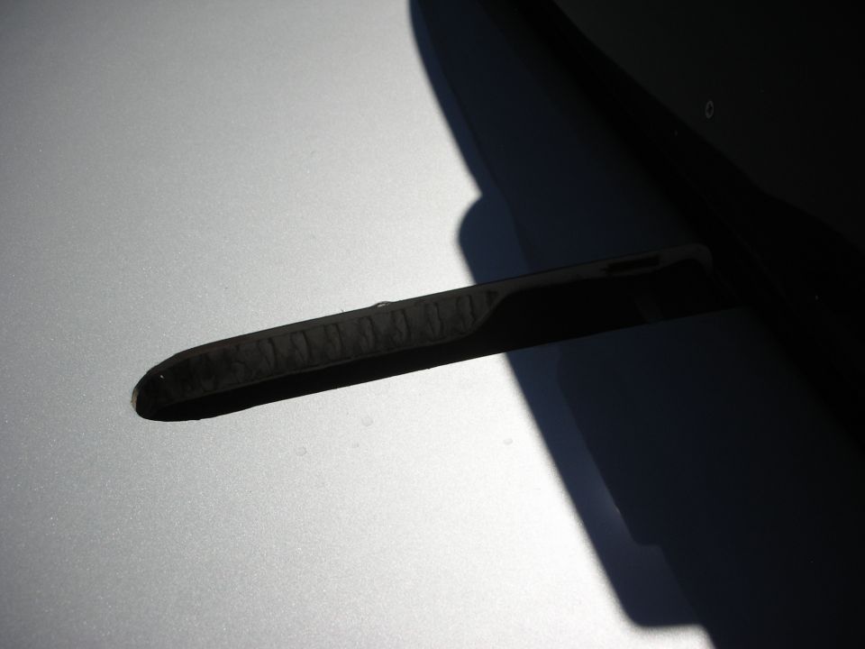 Black windshield wiper resting on a silver hood in bright sunlight