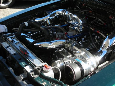 1998 Ford Crown Victoria - engine bay packed with mirror-polished turbo piping, blue anodized fittings, and a belt-driven supercharger in a green car.