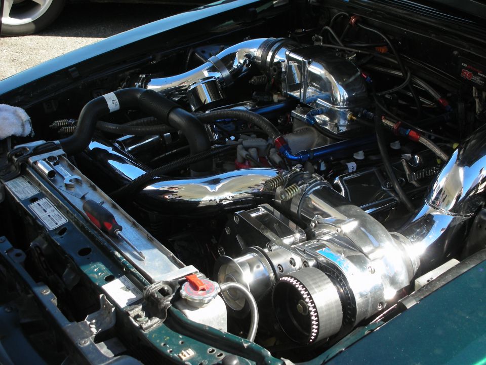 Polished turbo plumbing and supercharger in a green car engine bay