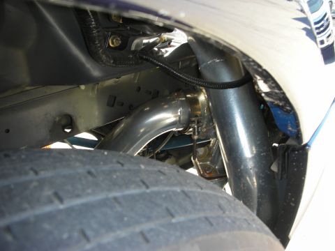 1998 Ford Crown Victoria - under-fender view showing polished stainless exhaust piping routed behind a wide rear drag slick on a light-colored car.