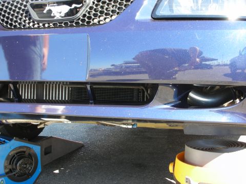 1998 Ford Crown Victoria - lower front fascia of a blue Mustang on jack stands, exposing an oil cooler core and intercooler piping behind the bumper.