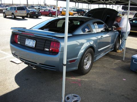 1998 Ford Crown Victoria - Rear three-quarter view of a light blue S197 Mustang coupe with its hood raised under a canopy at a track, drag wheels fitted.