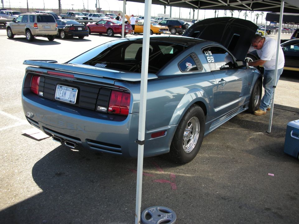 Rear of a light blue S197 Mustang with hood up under a canopy