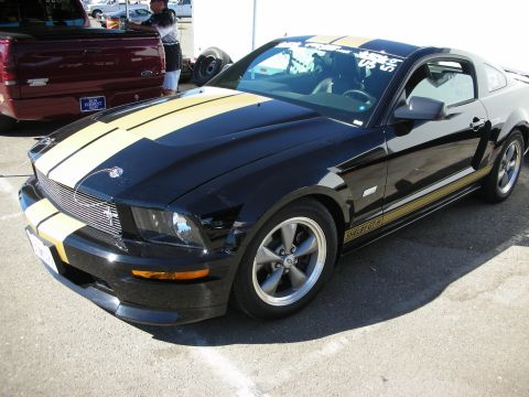 1998 Ford Crown Victoria - black S197 Shelby GT Mustang coupe with gold over-the-top racing stripes and gray five-spoke wheels parked in a lot.