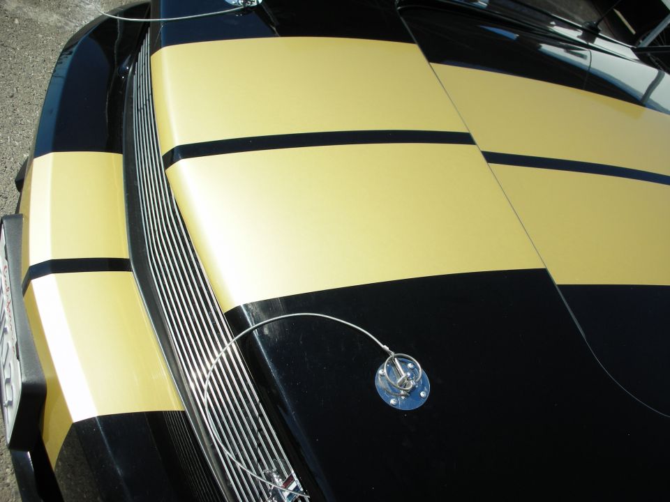Hood detail of a black Mustang with gold stripes and twist hood pin