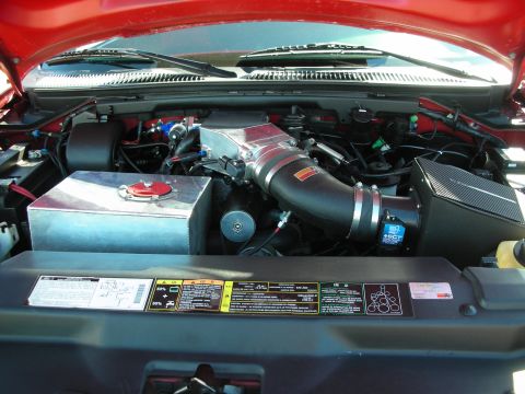 1998 Ford Crown Victoria - red truck's engine bay showing an aftermarket intake tube, a carbon-fiber airbox, an aluminum tank, and an under-hood emissions decal.