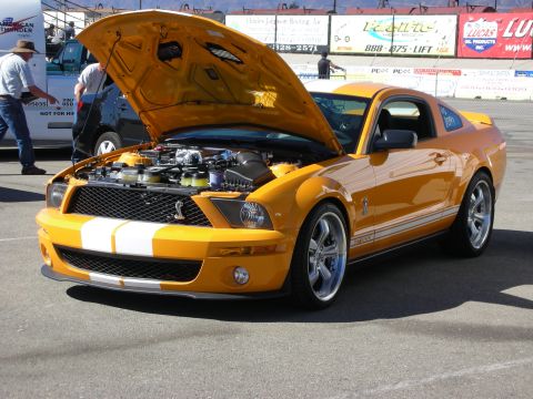 1998 Ford Crown Victoria - orange S197 Shelby GT500 Mustang with white racing stripes and chrome wheels sits with its hood open at an outdoor event.