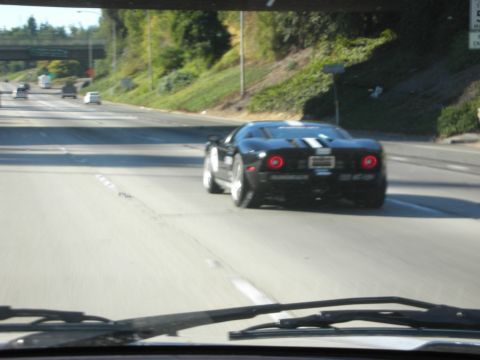 1998 Ford Crown Victoria - black mid-engine sports car with twin white stripes drives ahead on a multi-lane highway, photographed through a vehicle windshield.