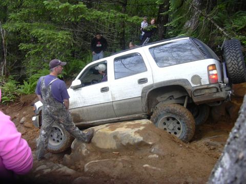 2002 GMC Yukon - A white SUV is shown attempting to climb over large rocks on a dirt trail.