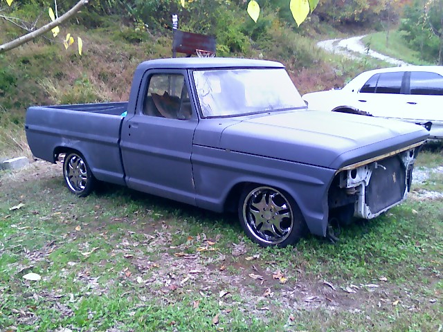 Gray Ford pickup truck with custom wheels, missing grille, parked on grass
