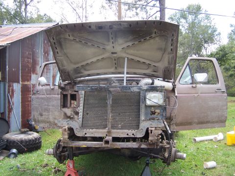 1981 Ford Bronco - The front end of a truck is disassembled, with the hood and doors open, revealing the engine bay and radiator area.