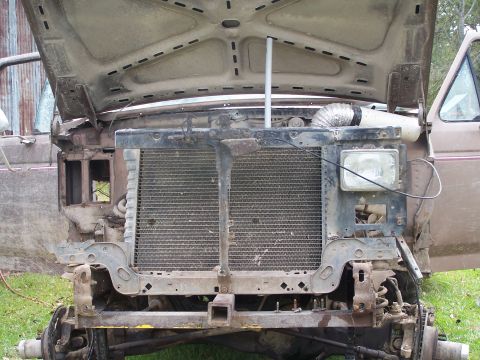 1981 Ford Bronco - The front of a damaged truck is shown with the hood up, revealing the radiator and engine bay.