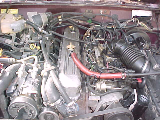 Engine bay of an inline-six with red heater hose and black intake tube