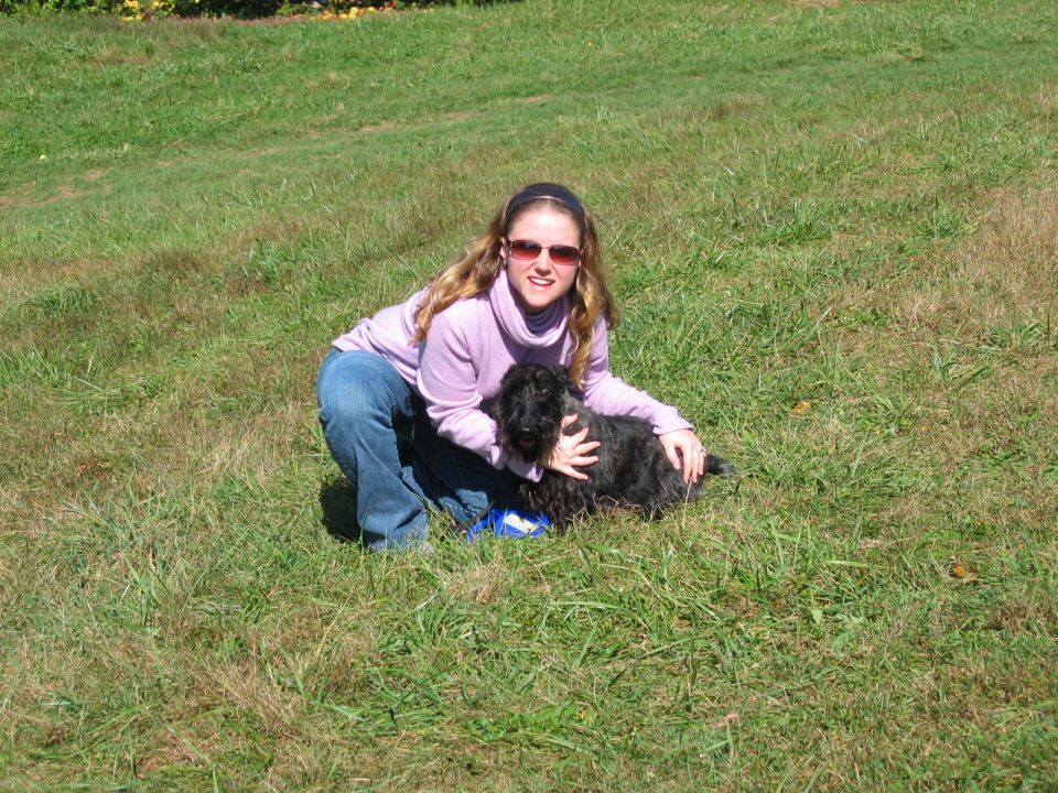 Woman crouching with a black dog in a grassy field