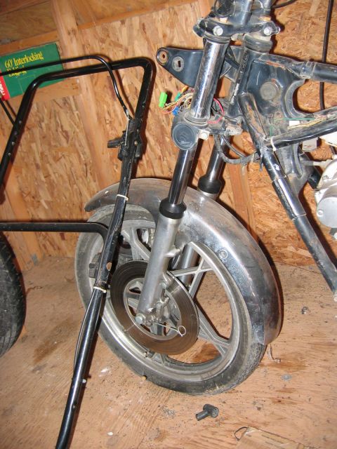 1985 Ford LTD Crown Victoria - Disassembled motorcycle front end with exposed wiring and a disc brake is visible.