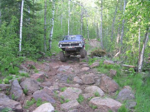 1977 Ford F-150 - A blue 1977 Ford F-150 tackles a challenging rocky trail, demonstrating its off-road capabilities.