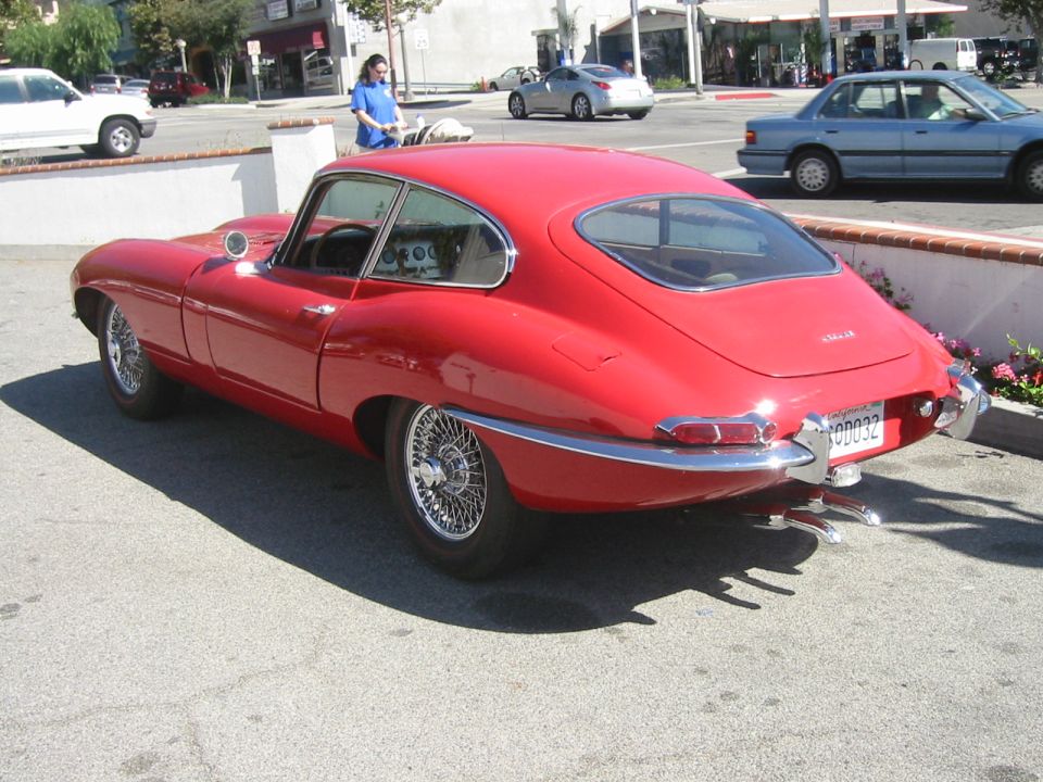 Red Jaguar E-Type coupe rear three-quarter view with wire wheels in a parking lot