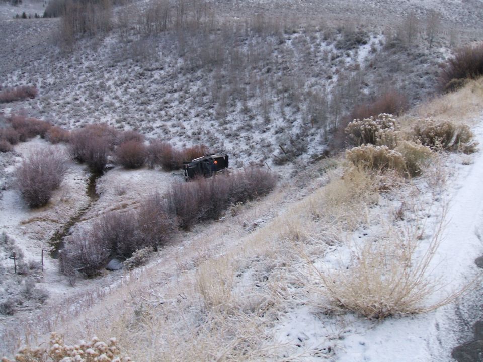 Black truck overturned on a snowy hillside next to brush