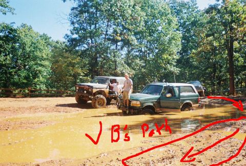 1996 Ford Bronco - Two off-road vehicles are stuck in a muddy area, with people standing around them.