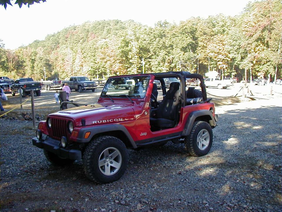 Red Jeep Wrangler Rubicon with doors and top removed at a gravel lot