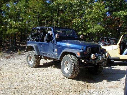 2005 Jeep Wrangler - Two Jeeps are parked on a dirt path surrounded by trees, suggesting an off-road adventure.