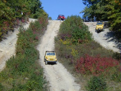 2005 Jeep Wrangler - Several Jeeps, including a yellow 2005 Wrangler, navigate an off-road trail on a sunny day.