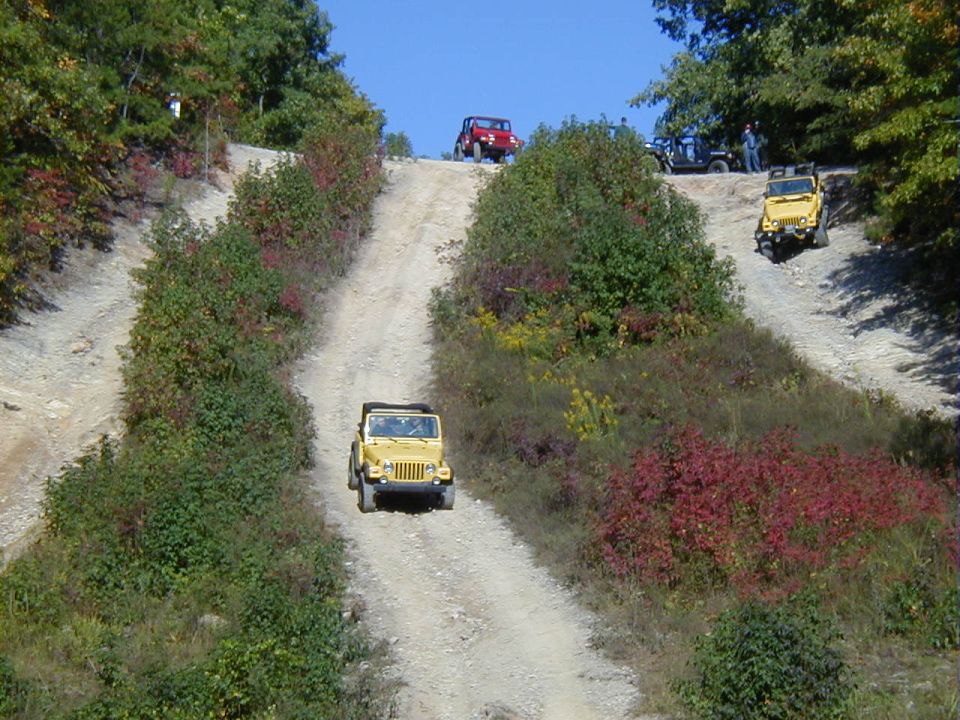 Yellow 2005 Jeep Wrangler driving up a dirt hill with other Jeeps behind it