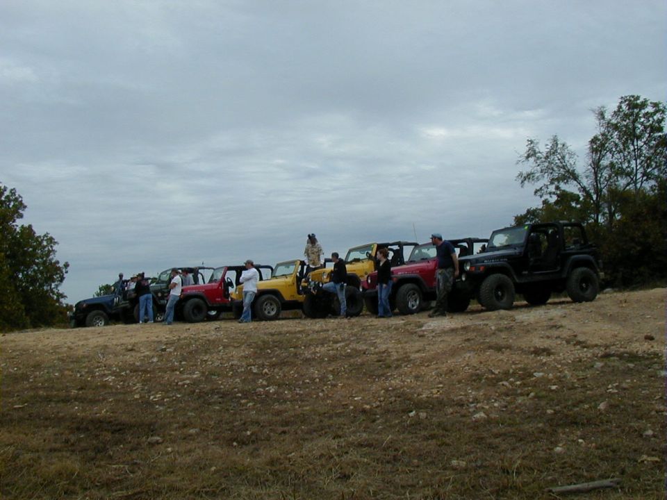 Several Jeep Wranglers parked in a line on a dirt hill under a cloudy sky. 2005 Jeep Wrangler is among them