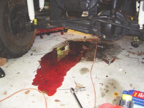 1986 Ford Bronco - A red fluid leak is visible under the vehicle's undercarriage, with tools scattered on the garage floor.