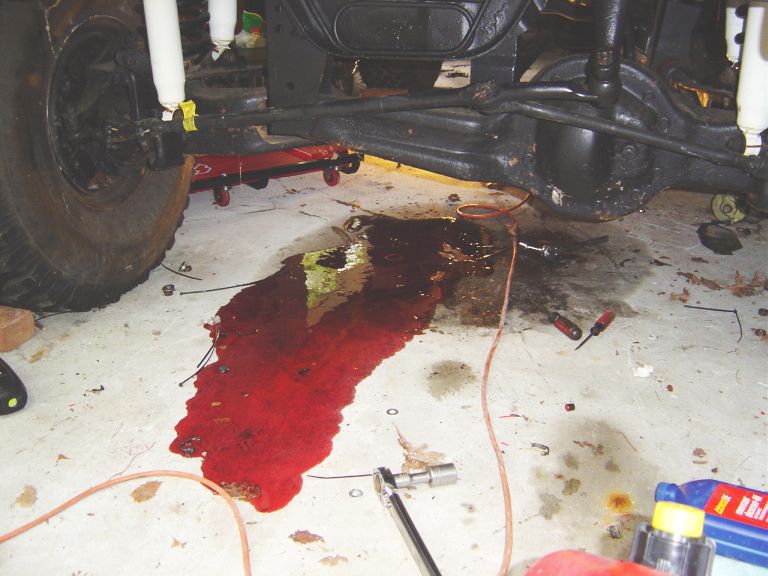 Pool of red fluid on garage floor under a lifted 4x4's solid front axle
