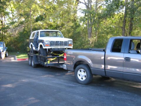 1986 Ford Bronco - A white Ford Bronco is loaded onto a trailer and towed by a pickup truck, with another vehicle in the background.