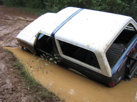 1986 Ford Bronco - A 1986 Ford Bronco is stuck in a muddy ditch, with its tires submerged in the brown water.