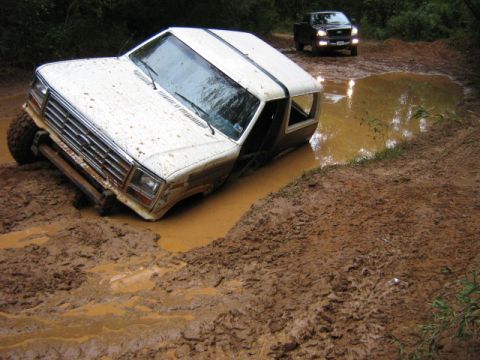 1986 Ford Bronco - An off-road adventure turns into a muddy predicament for this SUV, with another vehicle observing from behind.