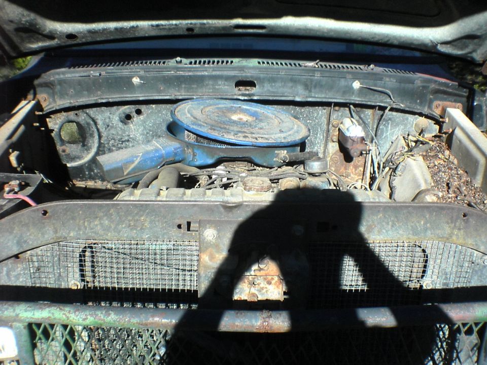 engine bay with blue air cleaner, rusty grille, and shadow of photographer