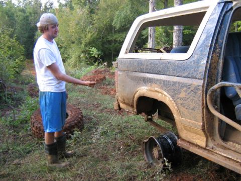1986 Ford Bronco - A man gestures near a heavily soiled SUV that is missing a rear wheel and tire.