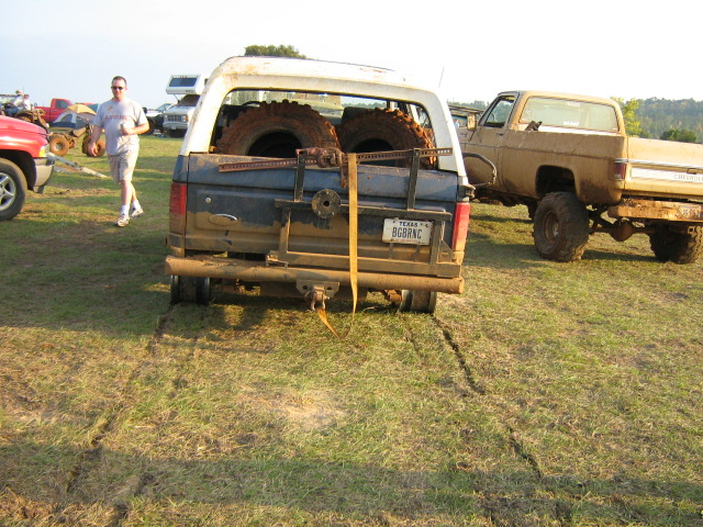 Rear of muddy blue and white Ford Bronco with spare tires in bed rack and Texas plate BGBRNC