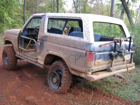 1986 Ford Bronco - This heavily modified Ford Bronco, likely from the early 1980s, is covered in mud and appears to be stuck off-road.
