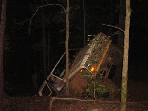1986 Ford Bronco - A white SUV is lodged precariously between trees after apparently going off-road.