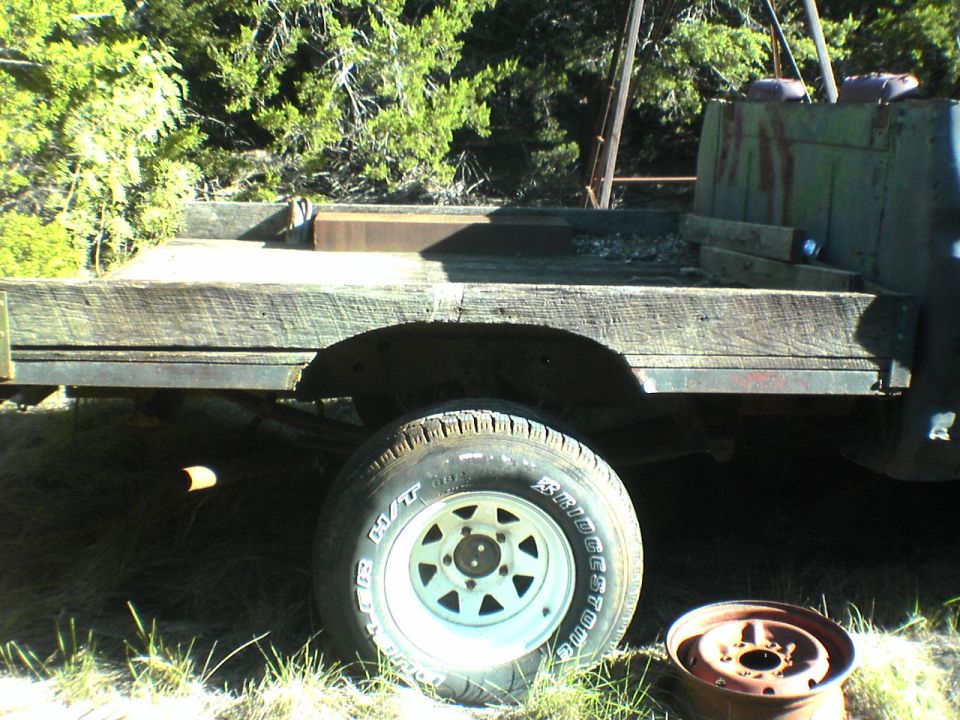 Side view of an old flatbed truck with wooden planks on the bed. Tire and wheel are visible