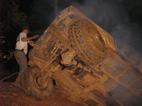 1986 Ford Bronco - A man attempts to right an overturned 1986 Ford Bronco that is heavily covered in mud.