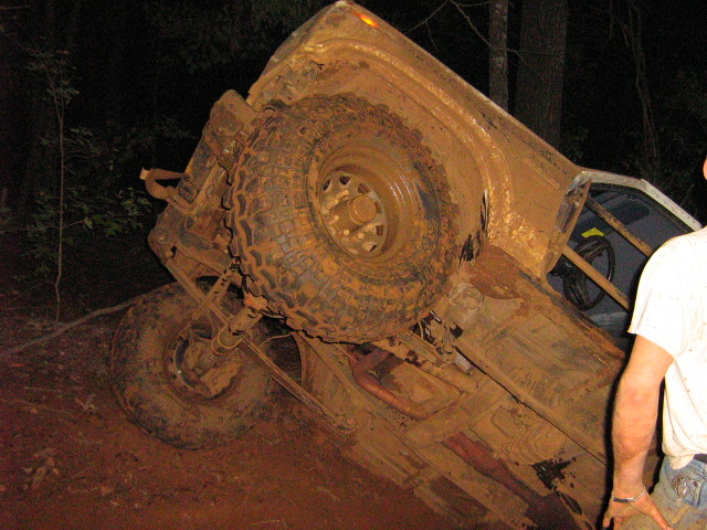 Mud-covered 4x4 rolled on its side at night showing undercarriage and spare tire carrier