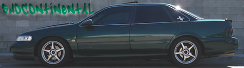 Dark green sedan with aftermarket wheels parked by a brick wall with graffiti
